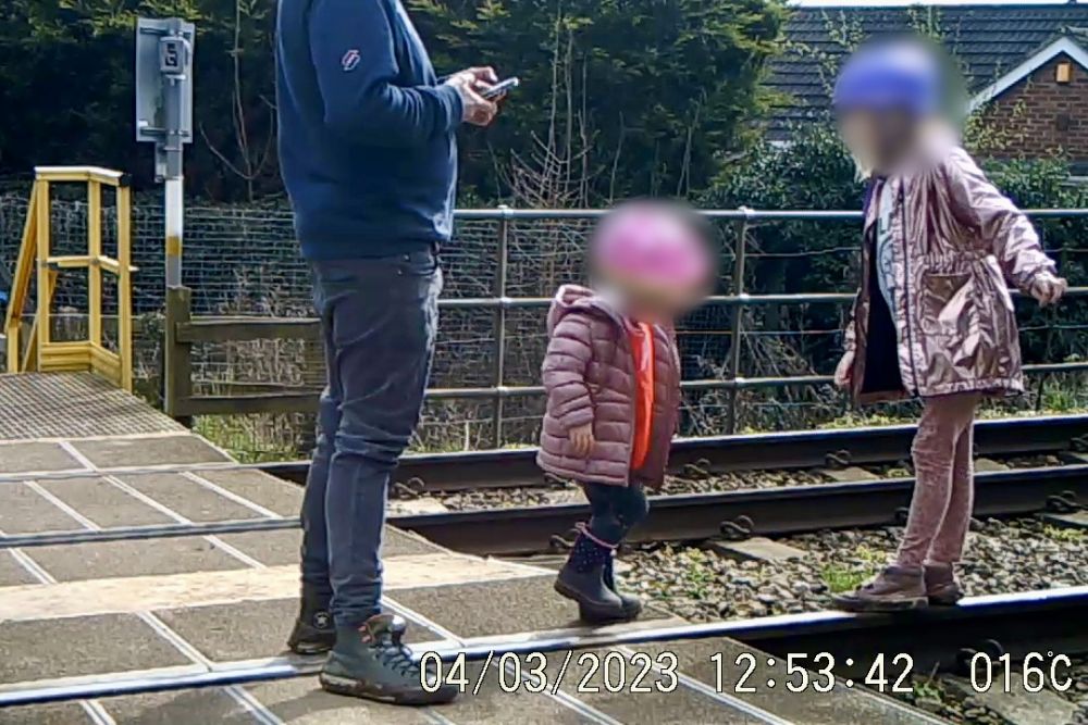a man with two little girls using the rails to play on pointing out the ‘pretty hills’ in the distance to them; they were caught on camera on the tracks for over a minute and a half © Network Rail